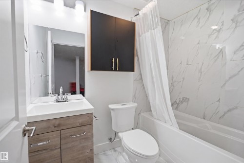 Full bathroom featuring a single vanity with wood-finish cabinetry, a white countertop basin, and a wall-mounted mirror - 1523 36 Avenue, Edmonton, AB - Indoor Photo Showing Bathroom