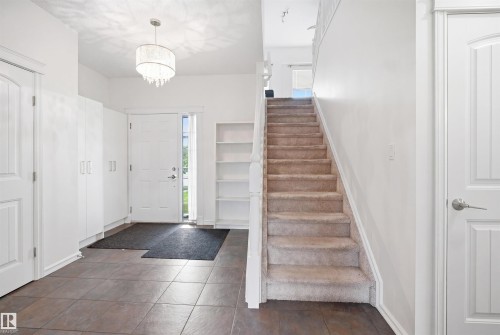Foyer featuring ceramic tile flooring, a staircase with carpeted treads, a crystal-style chandelier, white built-in cabinetry, and integrated shelving - 1523 36 Avenue, Edmonton, AB - Indoor Photo Showing Other Room
