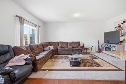 Spacious living area featuring light-toned walls, wood-finish flooring, and a large window providing natural light - 