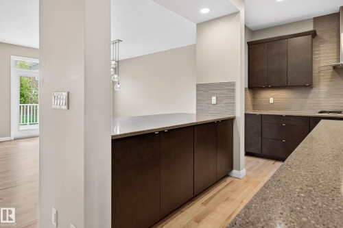 Contemporary kitchen featuring dark wood cabinetry, solid surface countertops, and a full-height tiled backsplash - 17838 60A Street, Edmonton, AB - Indoor Photo Showing Kitchen