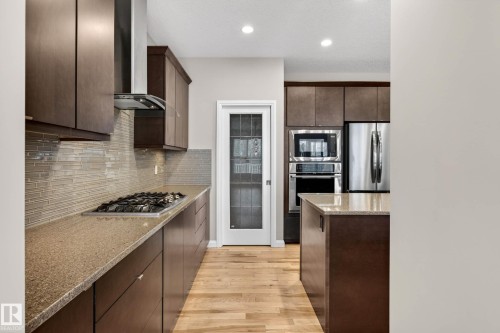Modern kitchen featuring dark wood-finish cabinetry, light wood-finish flooring, and recessed lighting - 17838 60A Street, Edmonton, AB - Indoor Photo Showing Kitchen With Upgraded Kitchen