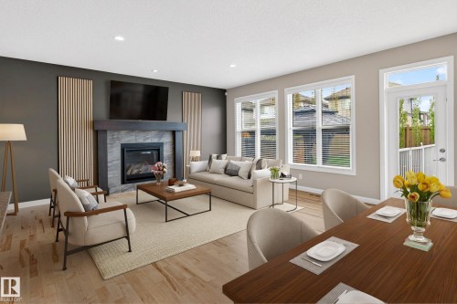 Open-concept living area featuring light wood-finish flooring, a contemporary fireplace with a dark wood mantel and stone surround, recessed lighting, and large windows with white trim - 17838 60A Street, Edmonton, AB - Indoor Photo Showing Living Room With Fireplace