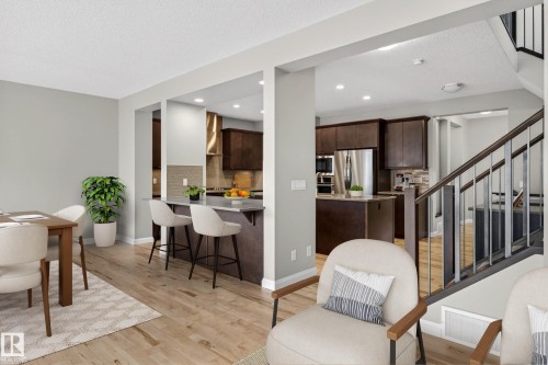 Open-concept living space featuring wood-finish flooring, a kitchen with dark wood cabinetry and stainless steel appliances, a breakfast bar with seating, a dining area, and a staircase with contemporary railings - 17838 60A Street, Edmonton, AB - Indoor