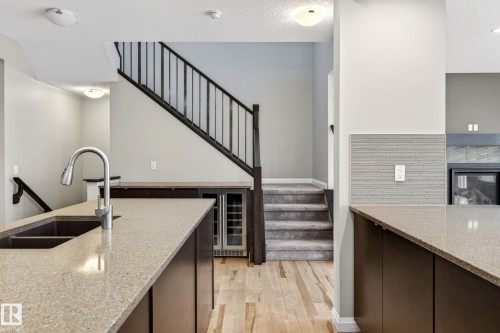 Kitchen island featuring a built-in sink with a gooseneck faucet, light speckled countertops, and dark wood-finish cabinetry - 17838 60A Street, Edmonton, AB - Indoor Photo Showing Kitchen With Double Sink