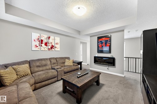 Carpeted living area featuring a built-in wall fireplace, light gray wall finishes, and a tray ceiling - 17838 60A Street, Edmonton, AB - Indoor Photo Showing Living Room With Fireplace