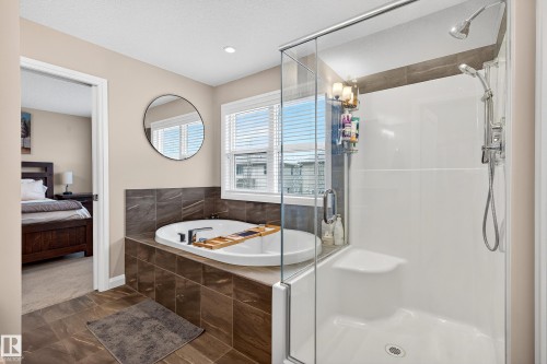 Modern bathroom featuring a built-in soaking tub with tile surround, a separate glass-enclosed shower with a built-in seat, and large format floor tiling - 17838 60A Street, Edmonton, AB - Indoor Photo Showing Bathroom