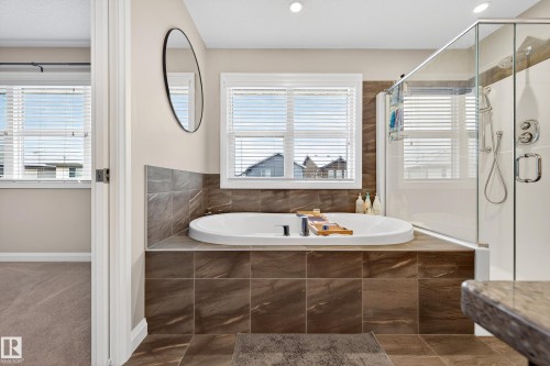 Contemporary bathroom featuring a built-in soaking tub with dark tile surround, a glass-enclosed shower, and dual windows with blinds - 17838 60A Street, Edmonton, AB - Indoor Photo Showing Bathroom