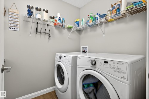 Dedicated laundry space featuring two front-loading machines, built-in wire shelving, and wood-finish flooring - 17838 60A Street, Edmonton, AB - Indoor Photo Showing Laundry Room