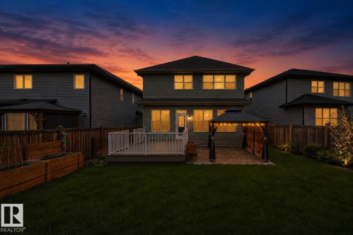 Expansive backyard featuring a manicured lawn, an elevated deck with white railings, and a paved patio area - 17838 60A Street, Edmonton, AB - Outdoor With Deck Patio Veranda With Exterior