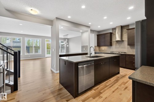 Modern kitchen featuring dark wood cabinetry, stainless steel appliances, and a central island with an integrated sink - 17838 60A Street, Edmonton, AB - Indoor Photo Showing Kitchen With Double Sink With Upgraded Kitchen
