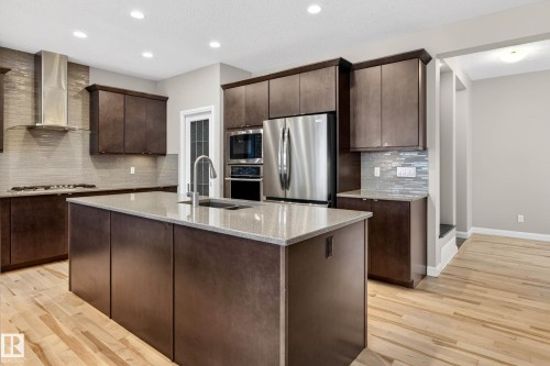 Spacious kitchen featuring dark wood cabinetry, light wood-finish flooring, and a large central island with an undermount sink - 17838 60A Street, Edmonton, AB - Indoor Photo Showing Kitchen With Upgraded Kitchen