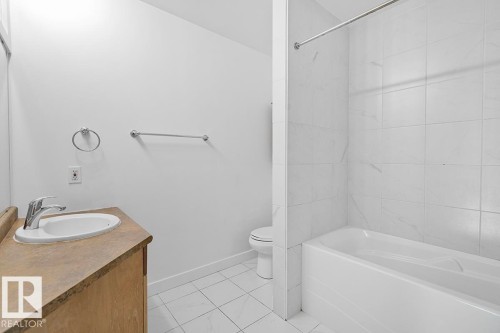 Bathroom featuring a vanity with an integrated sink, a chrome faucet, a white tub, and tiled walls and flooring - 117 10717 83 Avenue, Edmonton, AB - Indoor Photo Showing Bathroom