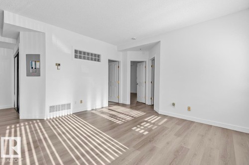 Spacious room featuring wood-finish flooring, white walls, and bright overhead lighting - 117 10717 83 Avenue, Edmonton, AB - Indoor Photo Showing Other Room