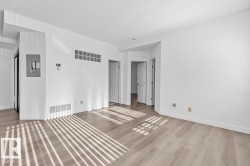 Spacious room featuring wood-finish flooring, white walls, and bright overhead lighting - 