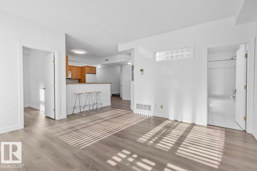 Spacious living area featuring wood-finish flooring, white walls, and a glass block transom window - 117 10717 83 Avenue, Edmonton, AB - Indoor