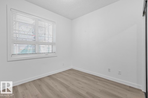 Room featuring wood-finish flooring, white baseboards, and a window with blinds - 117 10717 83 Avenue, Edmonton, AB - Indoor Photo Showing Other Room