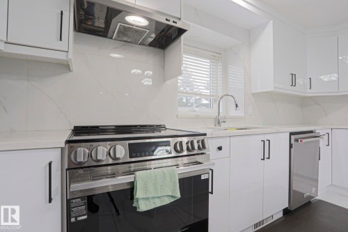 Modern kitchen featuring white cabinetry, stainless steel appliances, light-toned countertops, and a full-height backsplash - 313 Jillings Crescent, Edmonton, AB - Indoor Photo Showing Kitchen