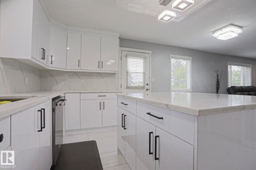 Kitchen featuring white high-gloss cabinetry with black hardware, white countertops, and a full-height backsplash - 313 Jillings Crescent, Edmonton, AB - Indoor Photo Showing Kitchen