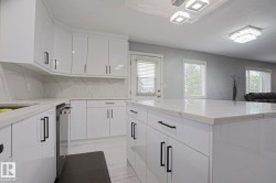 Kitchen featuring white high-gloss cabinetry with black hardware, white countertops, and a full-height backsplash - 