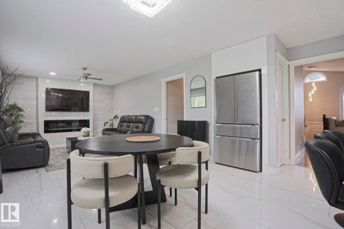 Open-concept living area featuring a modern fireplace, ceiling fan, stainless steel refrigerator, and light-toned tile flooring - 313 Jillings Crescent, Edmonton, AB - Indoor Photo Showing Dining Room With Fireplace