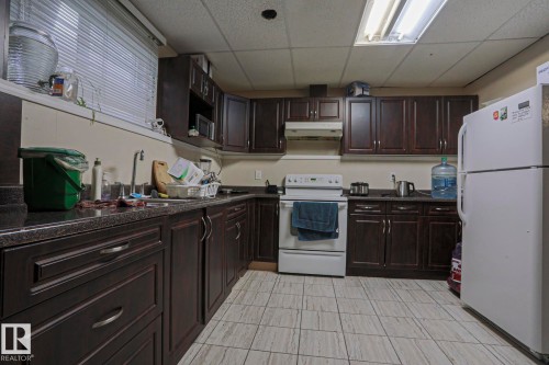 Kitchen featuring dark wood-finish cabinetry, solid surface countertops, a white electric range, and a white refrigerator - 313 Jillings Crescent, Edmonton, AB - Indoor Photo Showing Kitchen