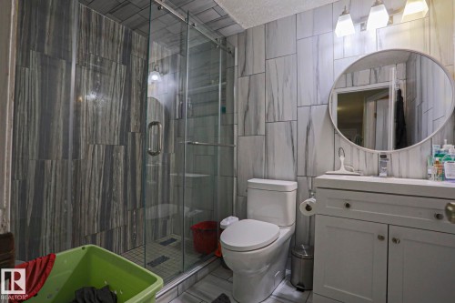 Full bathroom featuring a glass-enclosed shower with contrasting tile work, white vanity with integrated sink, contemporary round mirror, and tile flooring - 313 Jillings Crescent, Edmonton, AB - Indoor Photo Showing Bathroom