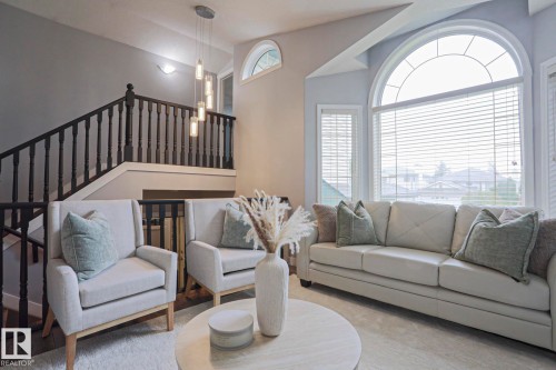 Living area featuring a large arched window with horizontal blinds, a white sofa, and two armchairs - 313 Jillings Crescent, Edmonton, AB - Indoor Photo Showing Living Room