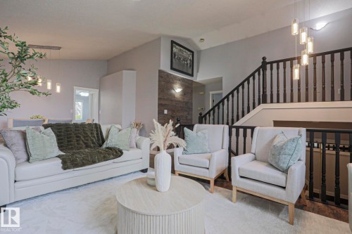 Spacious living area featuring a prominent staircase with dark wood balusters and railing, contemporary lighting fixtures, and a textured accent wall - 313 Jillings Crescent, Edmonton, AB - Indoor Photo Showing Living Room