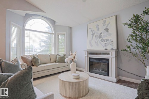 Living area featuring a prominent arched window, white window blinds, a built-in fireplace with a mantel, and wood-finish flooring - 313 Jillings Crescent, Edmonton, AB - Indoor Photo Showing Living Room With Fireplace