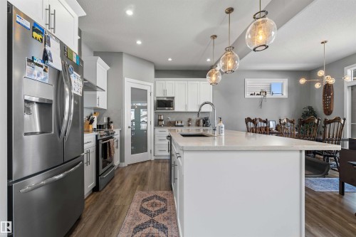 Kitchen featuring a white island with an undermount sink, stainless steel appliances, white cabinetry, wood-finish flooring, and recessed lighting - 524 Mcdonough Way, Edmonton, AB - Indoor Photo Showing Kitchen With Stainless Steel Kitchen With Upgraded Kitchen