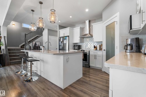 Modern kitchen featuring a central island with countertop seating, white cabinetry, stainless steel appliances, and wood-finish flooring - 524 Mcdonough Way, Edmonton, AB - Indoor Photo Showing Kitchen With Upgraded Kitchen