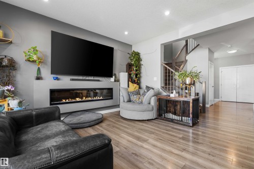 Living area featuring a linear electric fireplace, recessed lighting, wood-finish flooring, and a visible staircase with wooden handrails and balusters - 524 Mcdonough Way, Edmonton, AB - Indoor Photo Showing Living Room With Fireplace