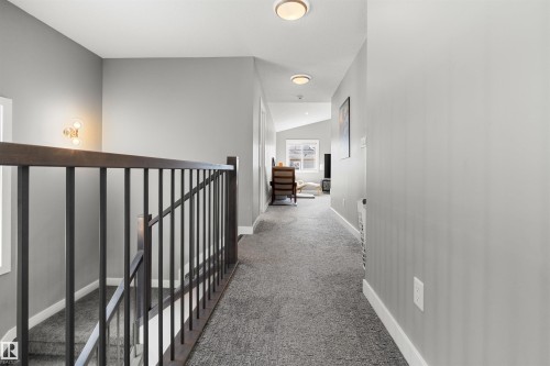 Carpeted hallway featuring a dark wood handrail with black metal balusters, contemporary flush-mount lighting, and light gray wall paint - 524 Mcdonough Way, Edmonton, AB - Indoor Photo Showing Other Room
