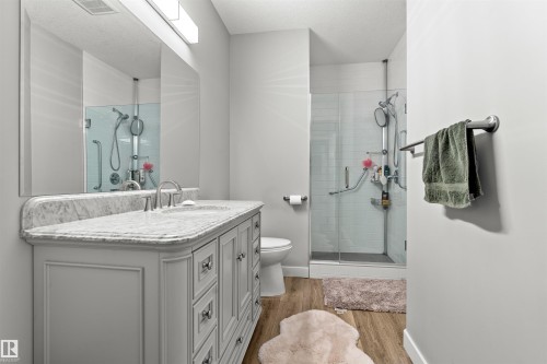 Bathroom featuring a white vanity with a light-colored countertop, an oversized mirror, a glass-enclosed shower, and wood-finish flooring - 524 Mcdonough Way, Edmonton, AB - Indoor Photo Showing Bathroom
