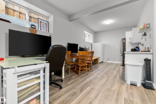 Versatile interior space featuring wood-finish flooring, light gray walls, recessed lighting, and a compact kitchen area with white cabinetry and a built-in stainless steel refrigerator - 524 Mcdonough Way, Edmonton, AB - Indoor Photo Showing Office