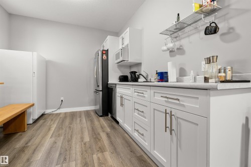 Contemporary kitchen featuring wood-finish flooring, light gray walls, white cabinetry with brushed nickel hardware, a white solid surface countertop, and stainless steel appliances - 524 Mcdonough Way, Edmonton, AB - Indoor Photo Showing Kitchen