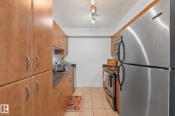 Galley kitchen featuring light wood-finish cabinetry, dark countertops, and stainless steel appliances including a refrigerator, microwave, and range - 