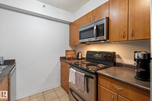 Kitchen featuring wood cabinetry, stainless steel microwave, black electric range, and dark countertops - 905 10303 105 Street Nw, Edmonton, AB - Indoor Photo Showing Kitchen