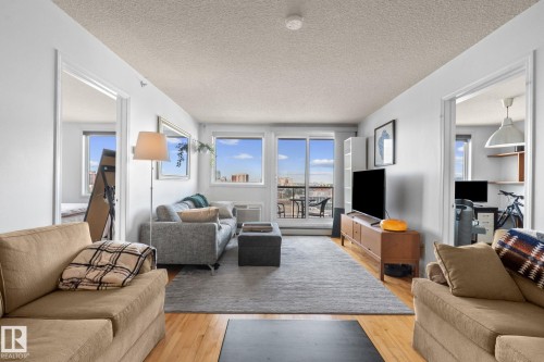 Living area featuring wood-finish flooring, a neutral color palette, and large windows with cityscape scenery - 905 10303 105 Street Nw, Edmonton, AB - Indoor Photo Showing Living Room