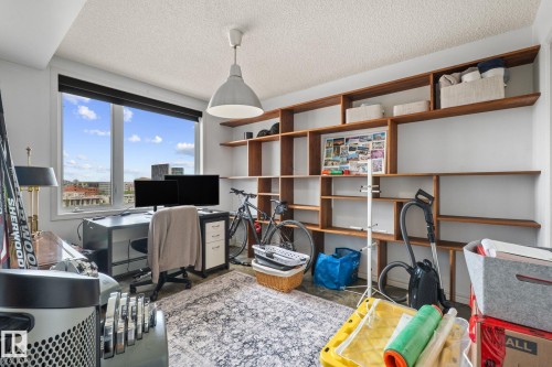 Expansive windows showcasing city views, textured ceiling, and a large custom built-in wood shelving unit - 905 10303 105 Street Nw, Edmonton, AB - Indoor Photo Showing Other Room