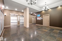 Spacious common area featuring textured tile flooring, two paneled elevators with stainless steel doors, and dual chandeliers - 