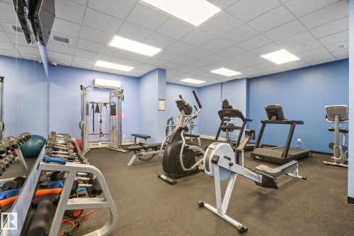 Dedicated fitness area featuring rubber flooring, drop ceiling with integrated lighting, mirrored wall, and wall-mounted air conditioning unit - 905 10303 105 Street Nw, Edmonton, AB - Indoor Photo Showing Gym Room