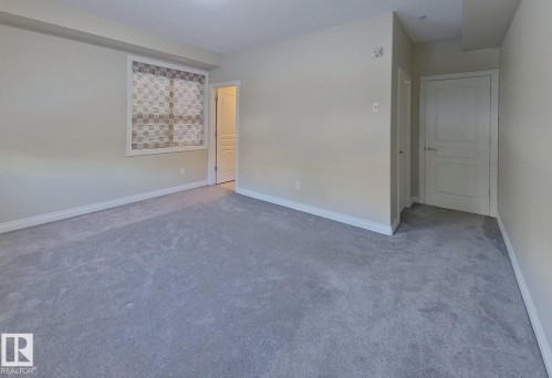 Spacious room featuring light gray carpeting, neutral wall paint, white baseboards, and a window with patterned blinds - 108 9603 98 Avenue Nw, Edmonton, AB - Indoor Photo Showing Other Room