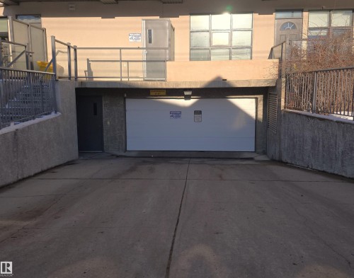Concrete driveway approach to a white garage door, featuring a concrete retaining wall with an iron fence - 108 9603 98 Avenue Nw, Edmonton, AB -  With Exterior