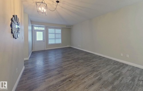 Spacious room featuring wood-finish flooring, light neutral wall tones, and a contemporary geometric pendant light fixture - 108 9603 98 Avenue Nw, Edmonton, AB - Indoor Photo Showing Other Room