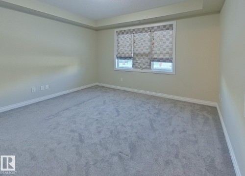 Spacious room featuring light gray carpeting, white baseboards, and a window with patterned blinds - 108 9603 98 Avenue Nw, Edmonton, AB - Indoor Photo Showing Other Room