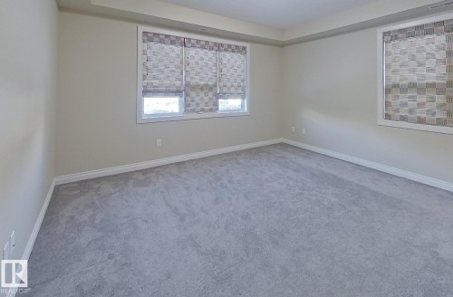 Spacious interior room featuring plush gray carpeting, neutral-toned walls, and white baseboards - 108 9603 98 Avenue Nw, Edmonton, AB - Indoor Photo Showing Other Room