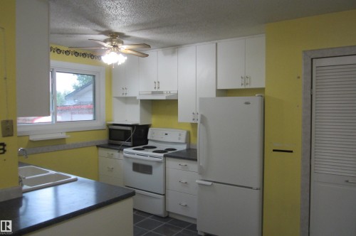 Kitchen featuring white cabinetry, dark countertops, a double basin sink, and a built-in range with an overhead microwave - 3814 37 Avenue, Leduc, AB - Indoor Photo Showing Kitchen With Double Sink