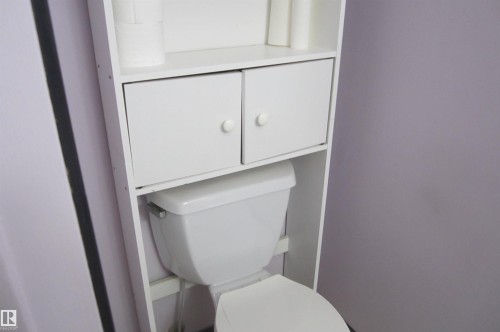White storage unit with two open shelves, two closed cabinets featuring round white knobs, and a white toilet - 3814 37 Avenue, Leduc, AB - Indoor