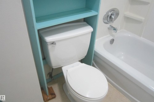 Bathroom featuring a white toilet, light blue built-in shelving, and a white bathtub with chrome fixtures - 3814 37 Avenue, Leduc, AB - Indoor Photo Showing Bathroom